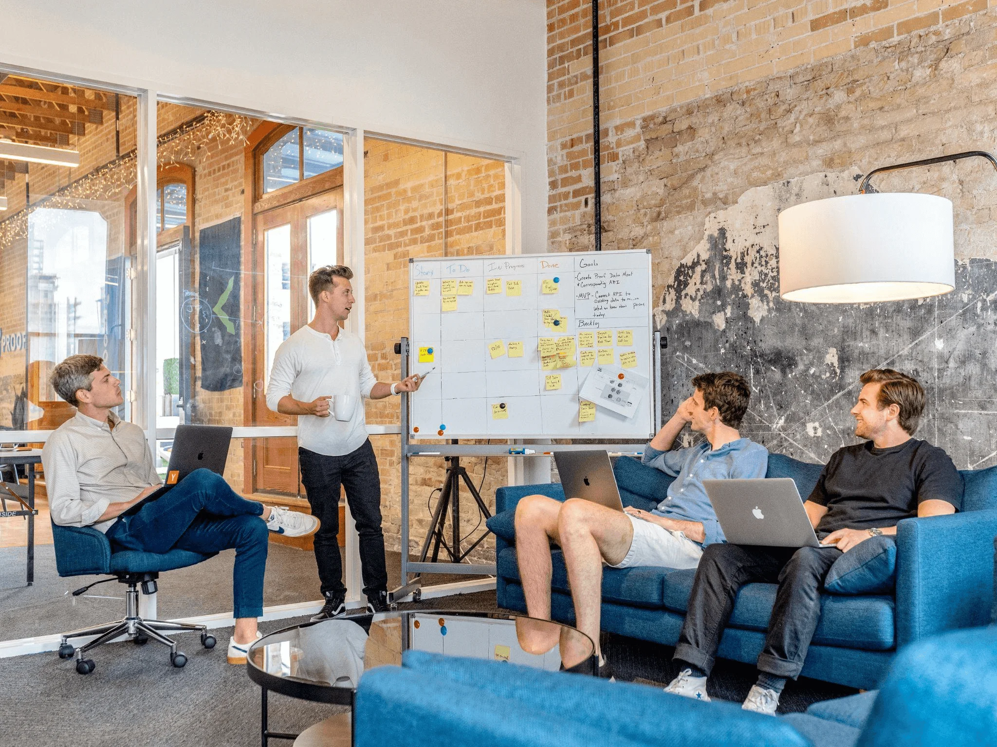 Team of professionals collaborating on laptops with a leader presenting strategy on a whiteboard, representing a business plan writing service.